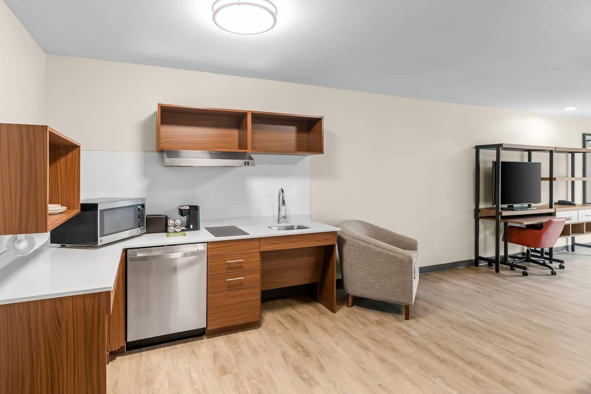 A compact kitchenette with a microwave, coffee maker, sink, and wooden cabinets.