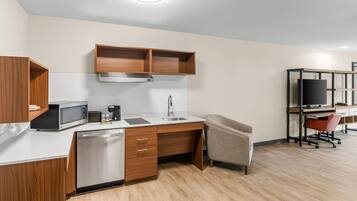 A compact kitchenette with a microwave, coffee maker, sink, and wooden cabinets.