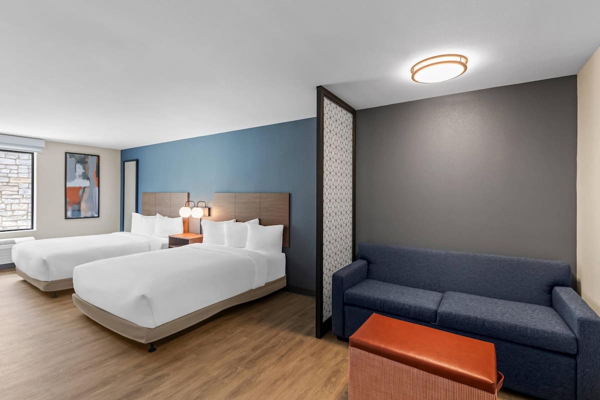 A hotel room with two beds, a sofa, a small table, and a decorative partition.