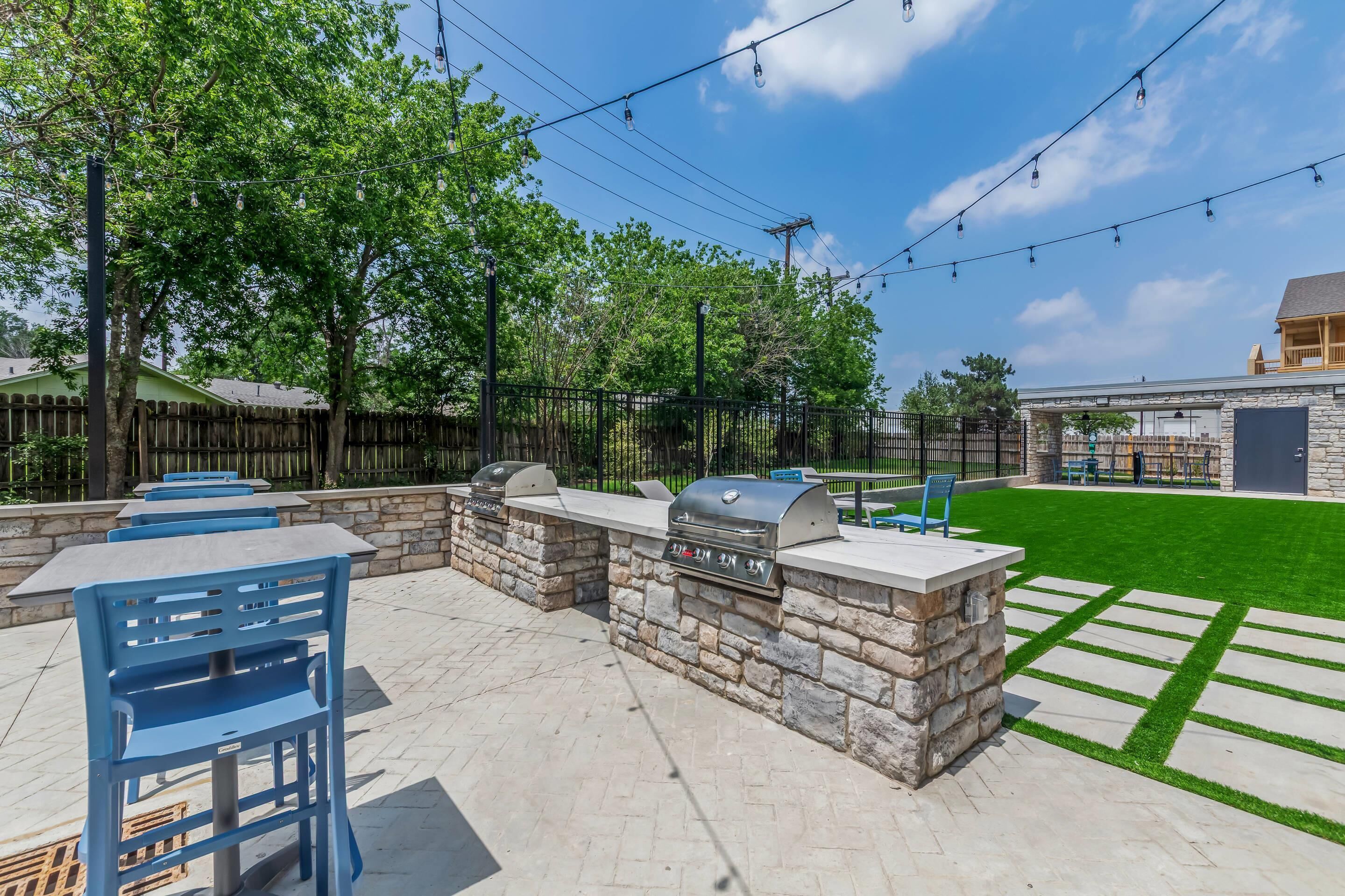 An outdoor patio with stone walls, barbecue grills, and blue chairs.