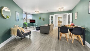 Ein modernes Wohnzimmer mit einem grauen Sofa, einem Esstisch mit Stühlen und einem Fernseher, der 'NETFLIX' anzeigt.