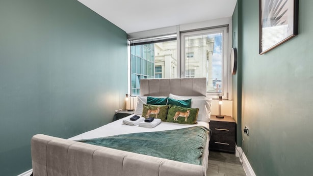 Ein Schlafzimmer mit Bett, Nachttisch, Fenster und einer Wandleuchte.