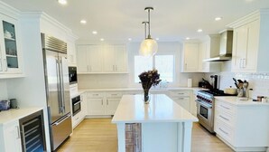 Una cocina moderna con armarios blancos, una isla central, electrodomésticos de acero inoxidable y una lámpara colgante.