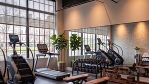 Une salle de sport équipée de tapis de course, d’haltères, de bancs et de grandes fenêtres.