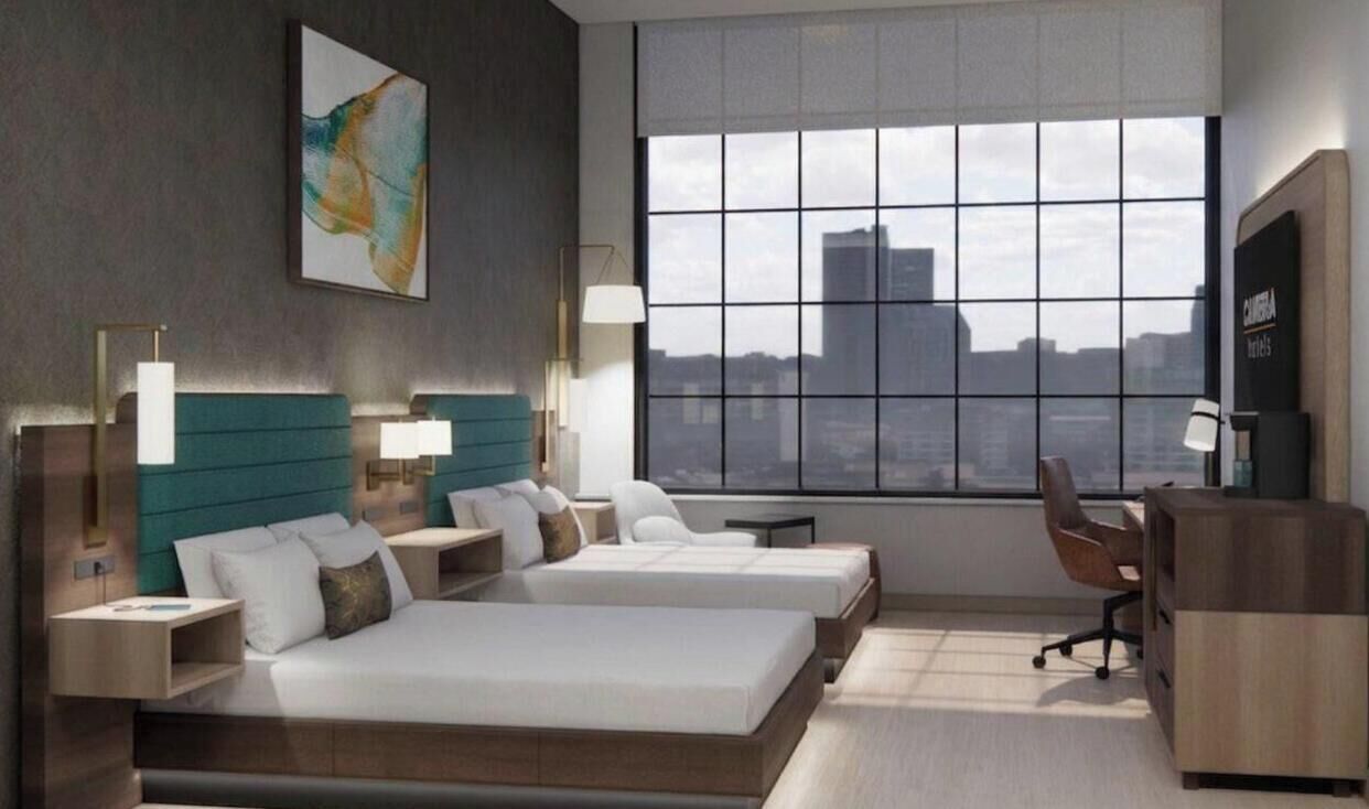 Ett modernt hotellrum med två sängar, ett skrivbord och ett stort fönster med utsikt över staden.