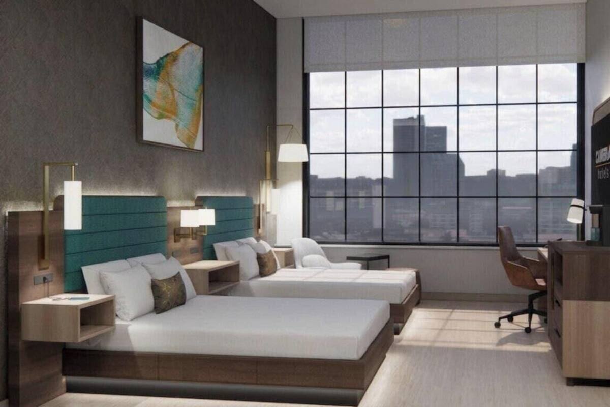 Una habitación de hotel moderna con dos camas, un escritorio y un amplio ventanal con vistas a la ciudad.