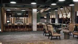 Un espace bar moderne, avec une enseigne CAMBRIA Hotels, des tabourets de bar et différents types de sièges, notamment des chaises et une table ronde.