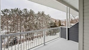 A covered balcony with a metal railing, overlooking a snowy landscape with trees and a mountain in the background. - Loft le Mercier by Gestion ELITE (Mont-Tremblant)