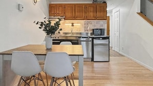 A compact kitchen with wooden cabinets, a dining table with chairs, and a small island with a plant. - Loft le Mercier by Gestion ELITE (Mont-Tremblant)