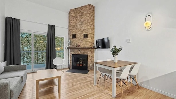 A modern living room with a fireplace, a dining table with chairs, a sofa, and a TV mounted on the wall. - Loft le Mercier by Gestion ELITE (Mont-Tremblant)