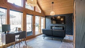 Ein modernes Wohnzimmer mit großem Fernseher, einer Couch, einem Schreibtisch mit Computer und einem Kamin.