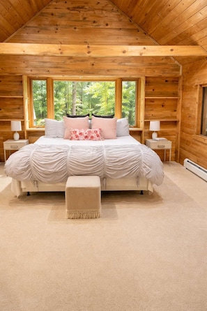 Un dormitorio con una cama grande, dos mesitas de noche y una ventana con vista a árboles.