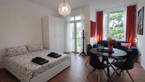 A bedroom with a bed, a dining table with chairs, a standing lamp, and a window with curtains. - Jewel on Lake Garda in Garda with Lake View (Garda)