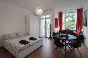 A bedroom with a bed, a dining table with chairs, a standing lamp, and a window with curtains. - Jewel on Lake Garda in Garda with Lake View (Garda)