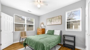 Ein Schlafzimmer mit Bett, Sessel, Schminktisch, Nachttisch und Deckenventilator.