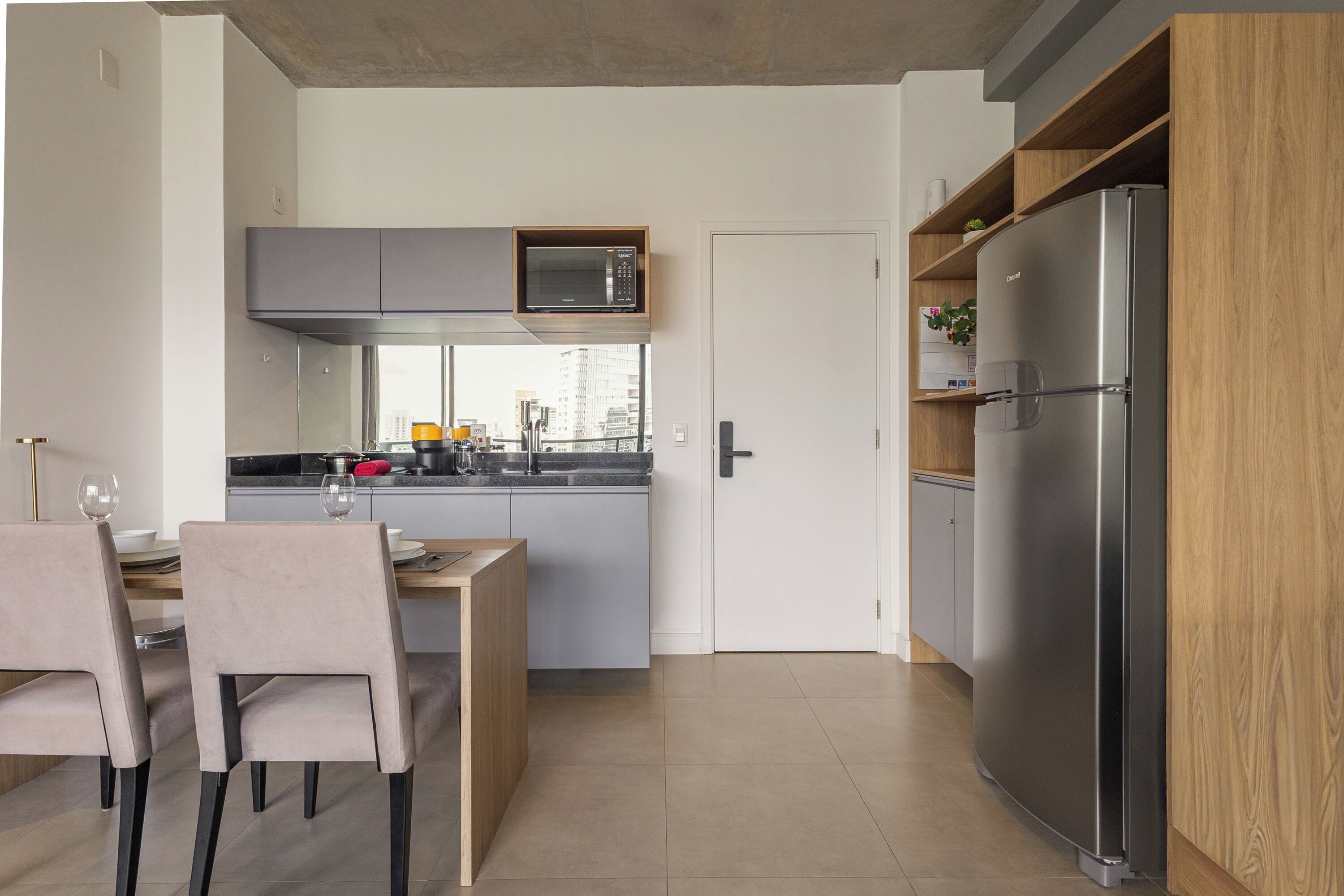 A modern kitchen with a built-in microwave, a stainless steel refrigerator, and a dining area with chairs and a table.