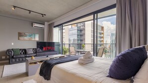 A modern hotel room with a large bed, a flat-screen TV, a sofa, and a balcony with a city view. - Luxo na Faria Lima - Millenium (São Paulo)