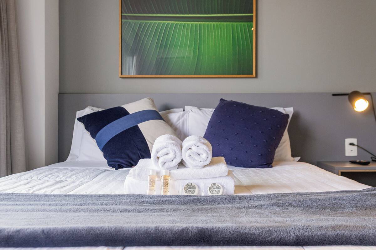 Een opgemaakt bed met handdoeken, een kussen en een flesje lotion.