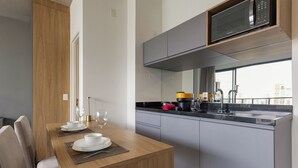 A modern kitchen with a dining area, featuring a wooden table set for two, a built-in microwave, and a large window offering a city view. - Luxo na Faria Lima - Millenium (São Paulo)