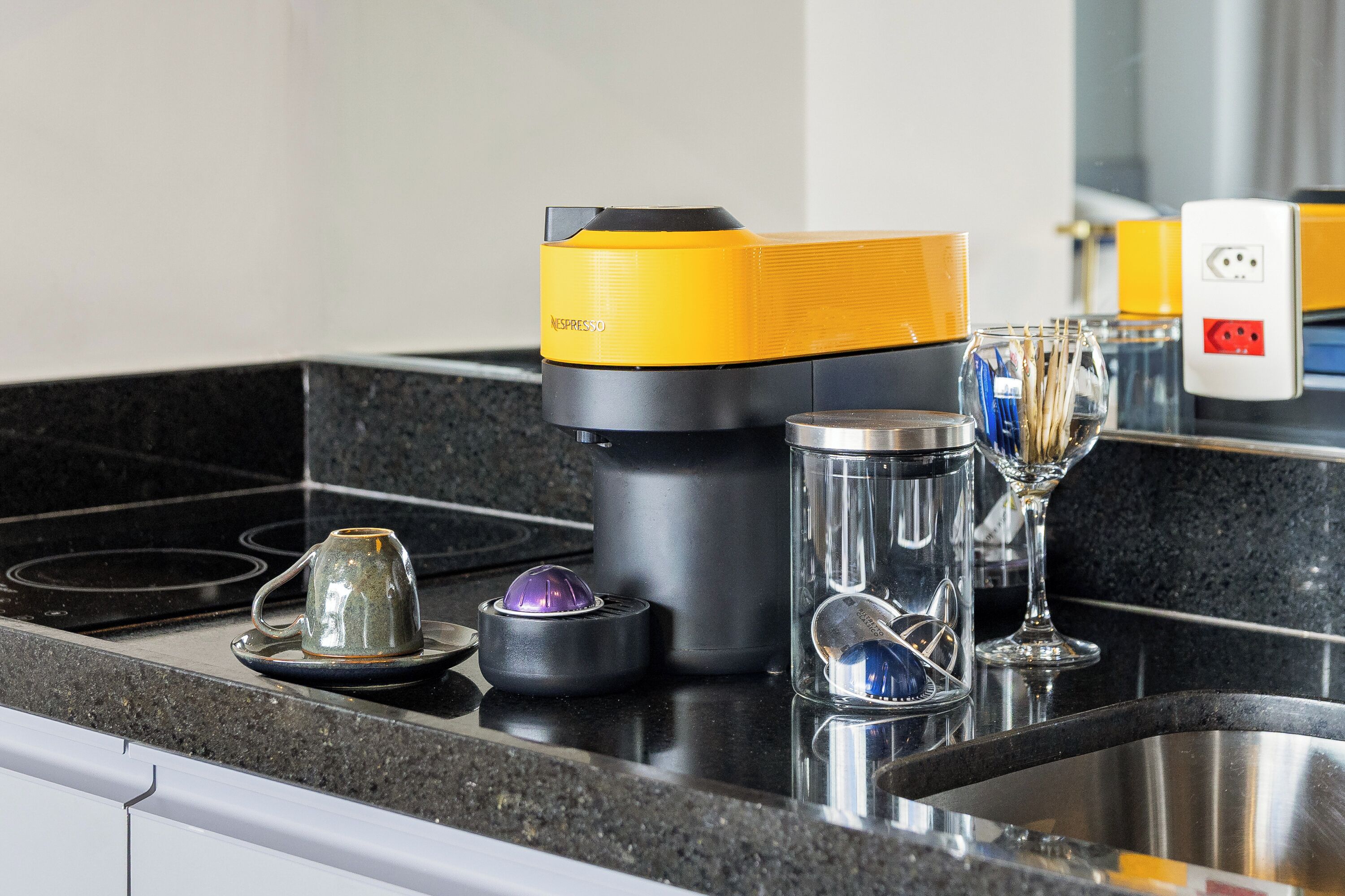 A kitchen counter with a coffee maker, a glass, and a wine glass.