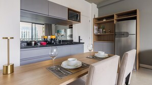 A modern kitchen with a built-in microwave, a stainless steel refrigerator, and a dining area with a wooden table set for two. - Luxo na Faria Lima - Millenium (São Paulo)