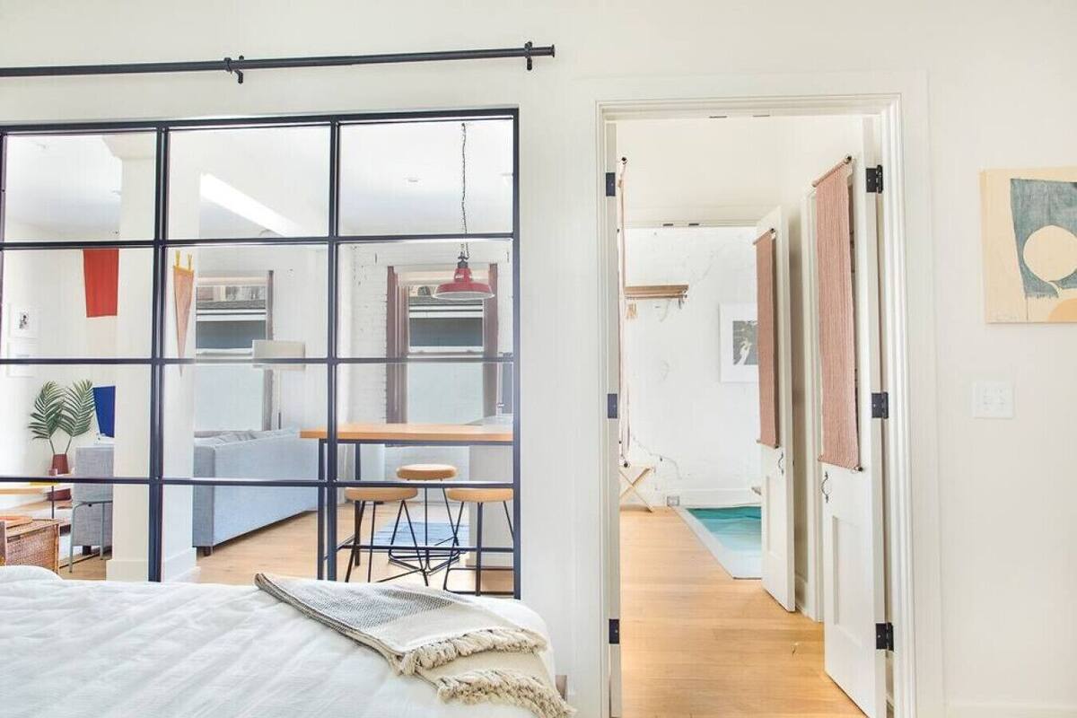 Un intérieur moderne avec une grande porte-fenêtre coulissante donnant sur un espace repas, un lit avec une tête de lit blanche et une piscine visible.
