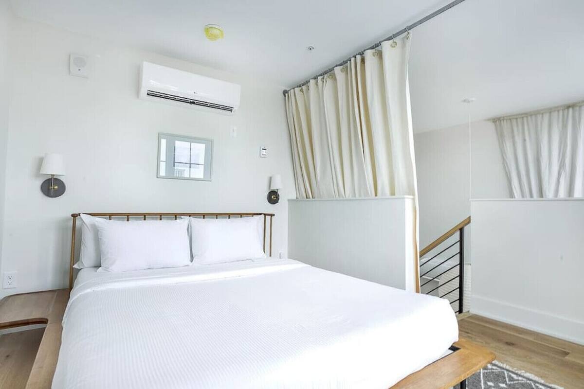 Une chambre d’hôtel avec un lit, une fenêtre, un appareil de climatisation, une lampe et un rideau.