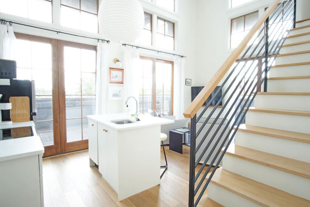 A modern kitchen with a central island, a built-in sink, and a staircase with wooden steps and metal railings.