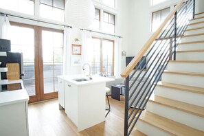 A modern kitchen with a central island, a built-in sink, and a staircase with wooden steps and metal railings. - The Windrose (Savannah)