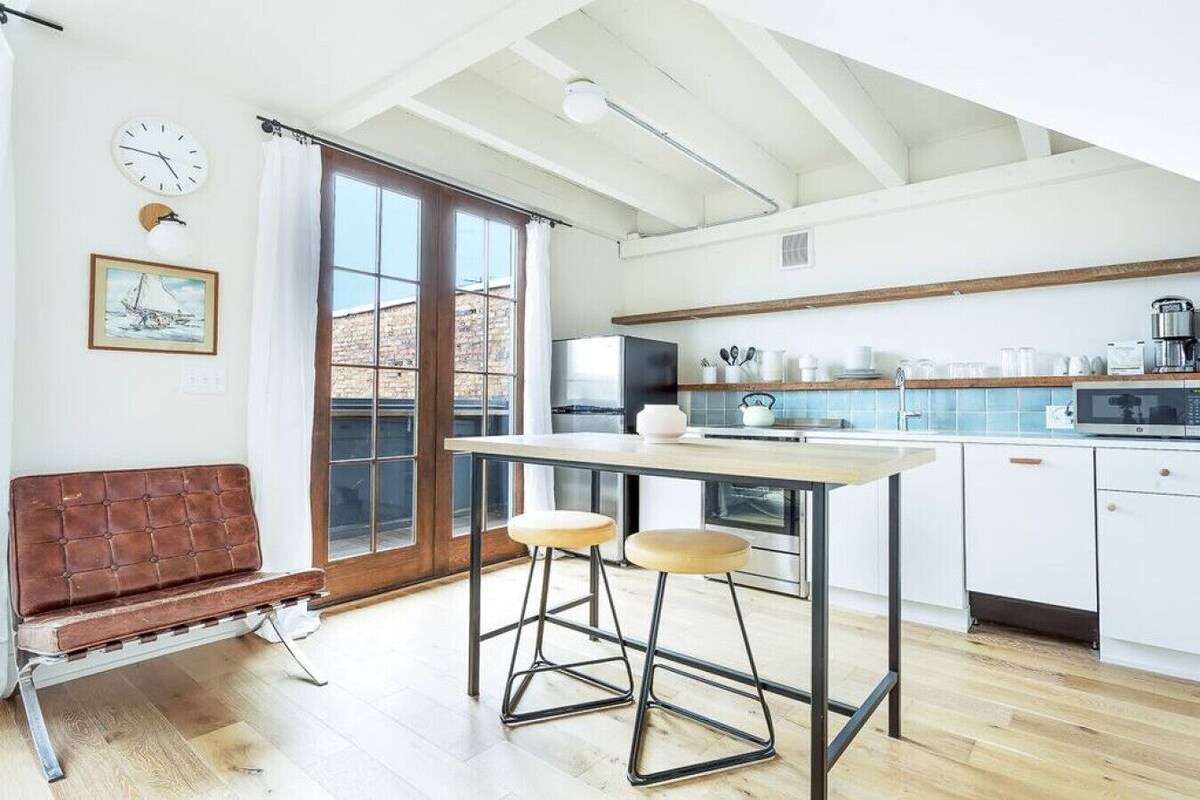 A modern kitchen with a large window, a dining area with stools, and a bench.