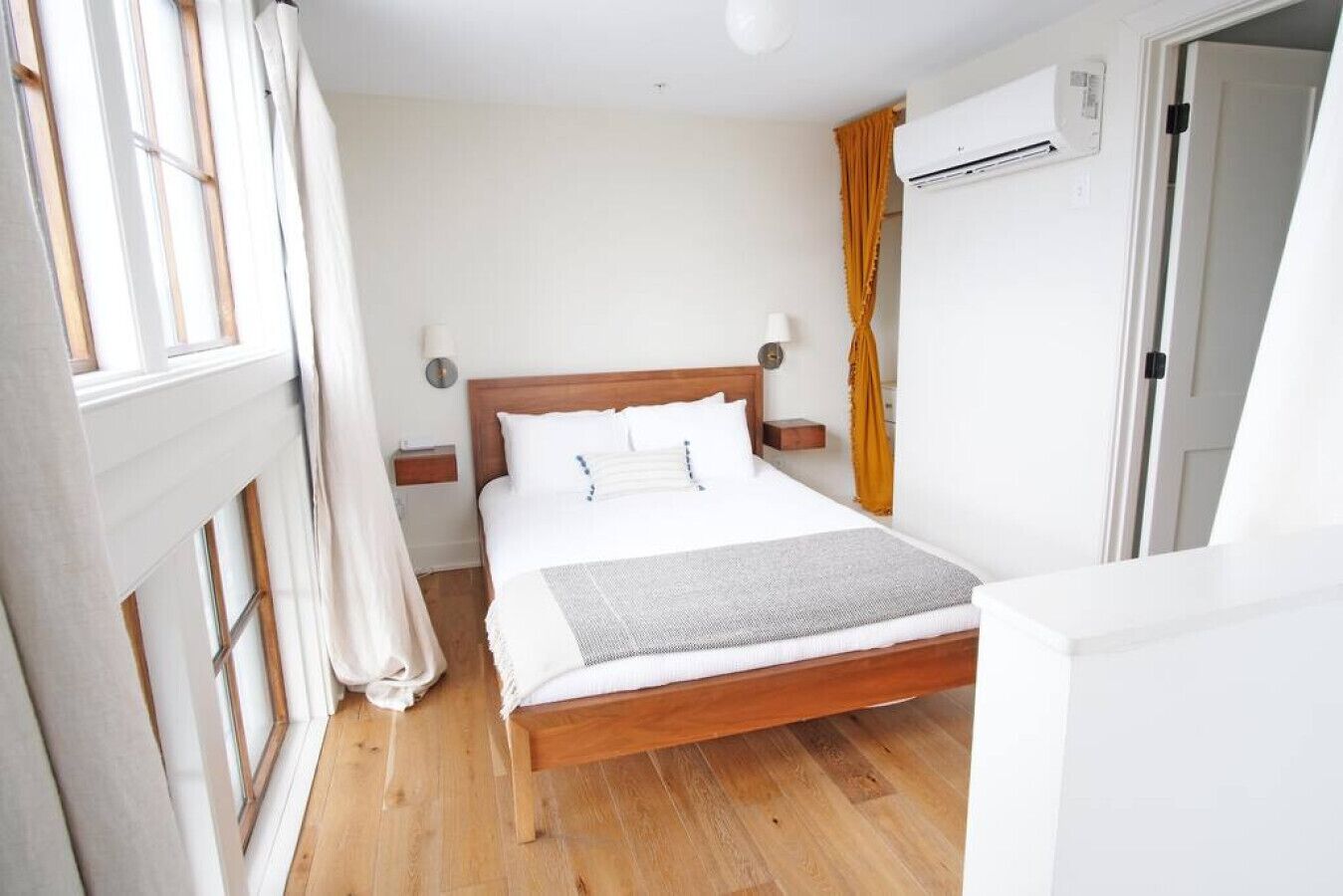 Een slaapkamer met een houten bed, witte beddengoed, een nachtkastje, een lamp en een airconditioning.