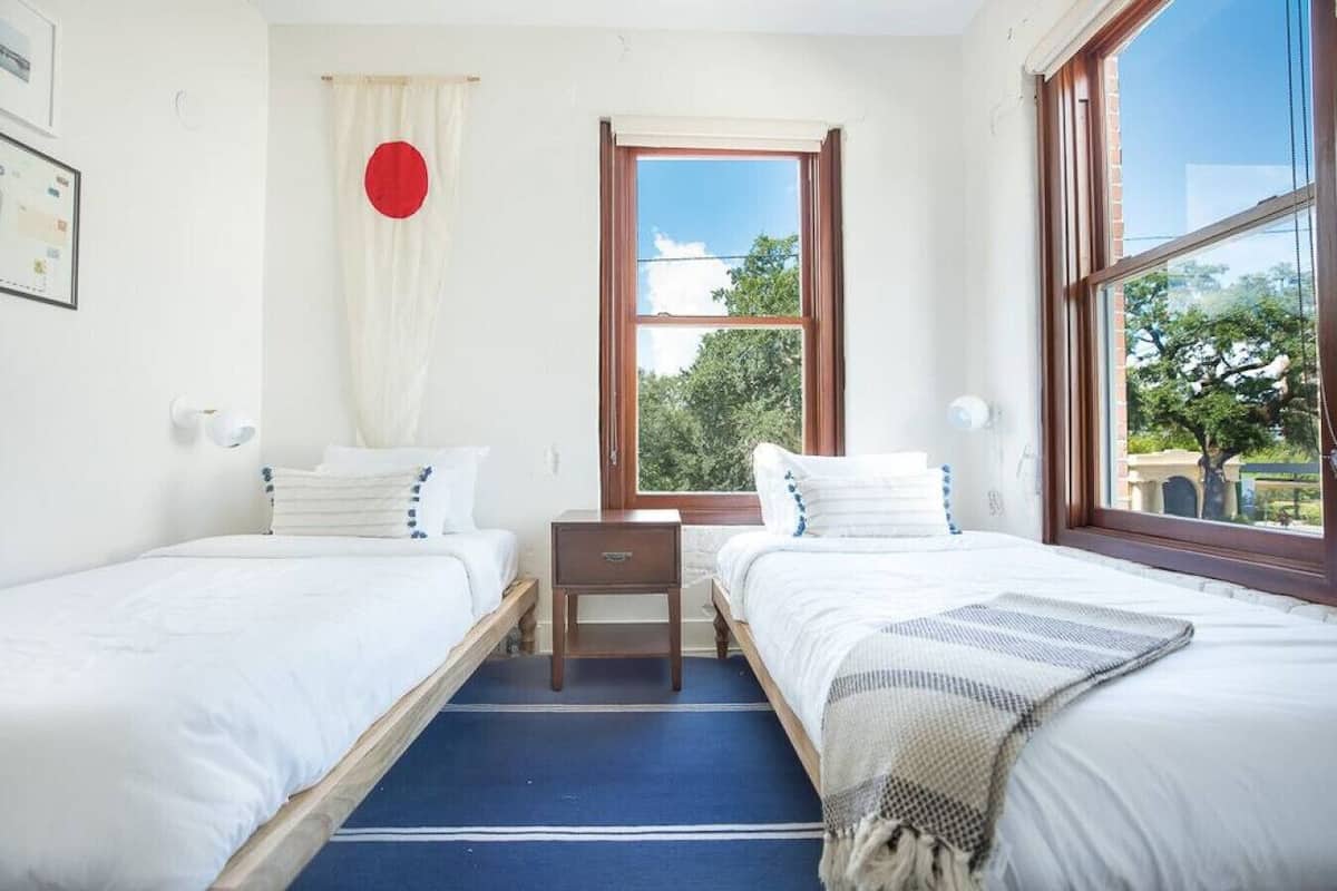 Une chambre avec deux lits, une fenêtre donnant sur des arbres et un motif circulaire rouge sur le mur.