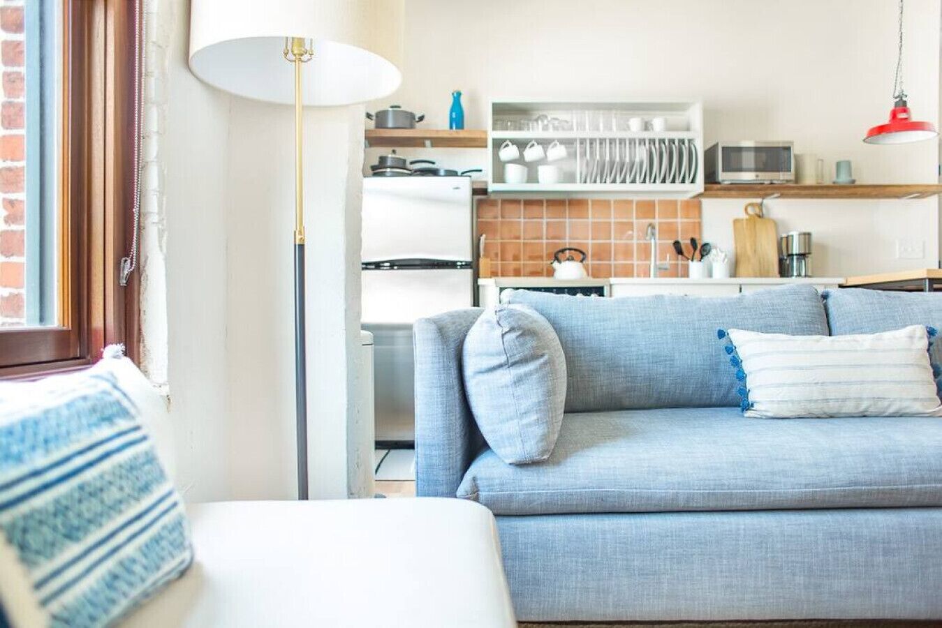 A modern living room with a sofa, a lamp, and a kitchen area in the background.