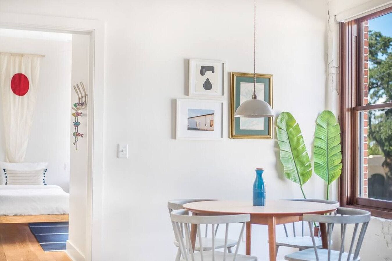 A bright room with a bed, a round table with chairs, and a window with a view of trees.