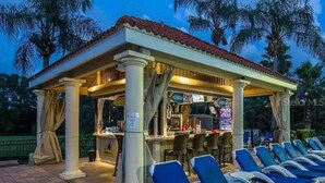 Un espacio al aire libre techado con área de bar, sillones de descanso y palmeras al fondo.