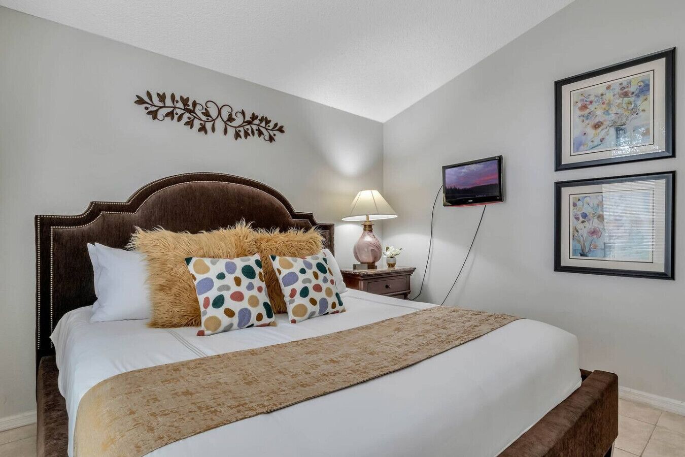 A neatly made bed with a brown headboard, a bedside lamp, and a TV on the wall.