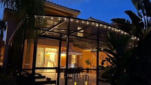 Une maison moderne dotée d’un espace extérieur couvert comprenant une table et des chaises, le tout agrémenté de plantes et créant une ambiance chaleureuse et accueillante.