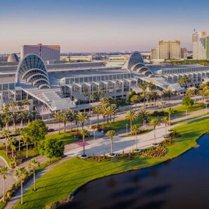 A modern building with a glass facade and curved roof structures, surrounded by palm trees and a water body. - 1206-H • 2 King Luxury • Epic/Universal/Disney (Orlando)
