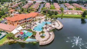 Luchtbeeld van een resort met diverse zwembaden, een waterpark en een steiger die in een meer uitloopt.