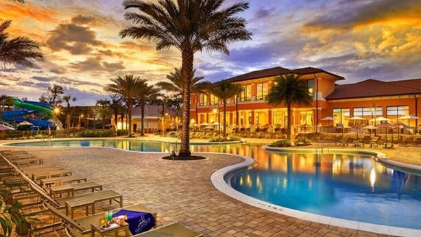Zwembad van een resort met ligbedden, een palmboom en een gebouw met een rood dak.