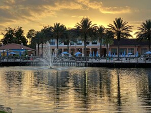 A waterfront hotel with a fountain, palm trees, and outdoor seating under umbrellas. - #2696 Lakefront Paradise Priv Spa Pool Disney Epic (Kissimmee)