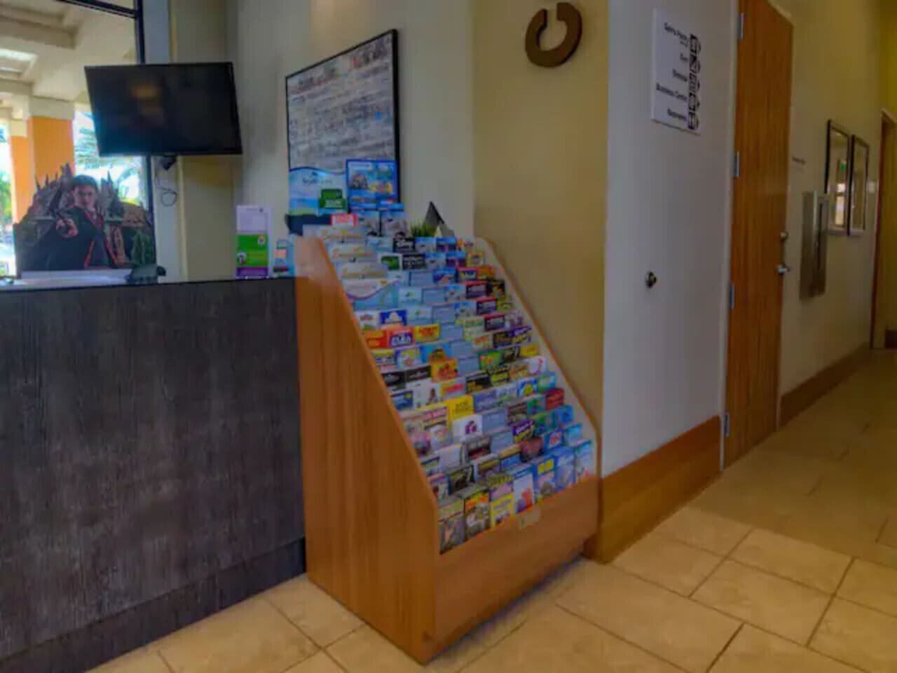A reception area with a desk, a wall-mounted TV, a poster, and a display of postcards.