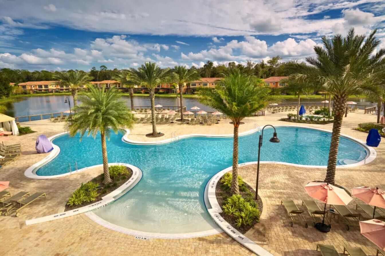 A resort pool area with a curved pool, palm trees, and lounge chairs.