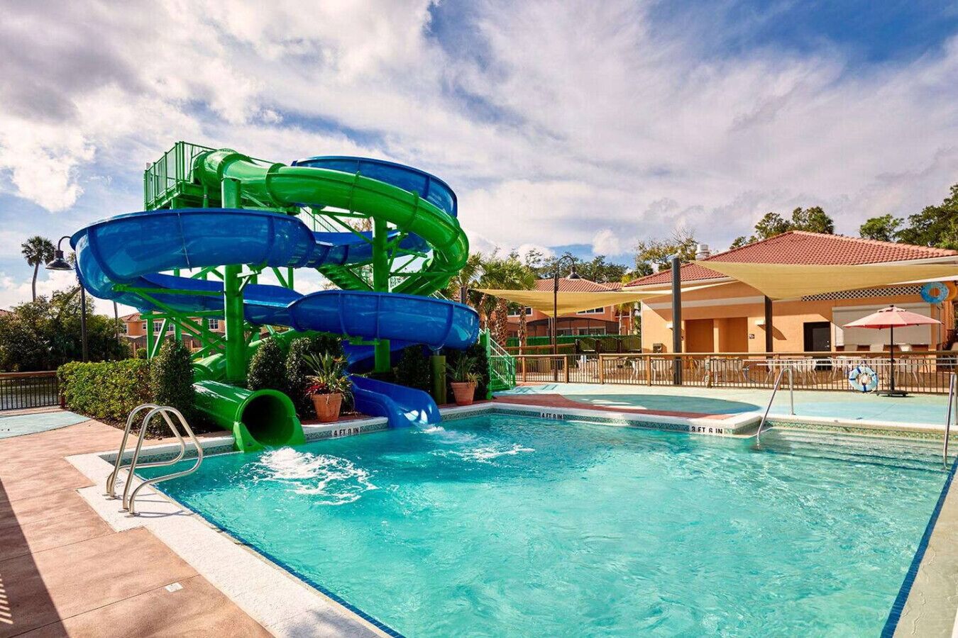 A pool with a water slide, a lifeguard stand, and a poolside area with umbrellas.
