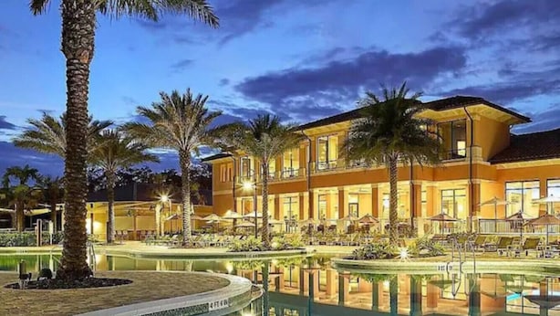 A hotel with a pool, palm trees, and a well-lit outdoor area at dusk. - #2662 Resort Theme Villa Priv Spa Disney Universal (Kissimmee)