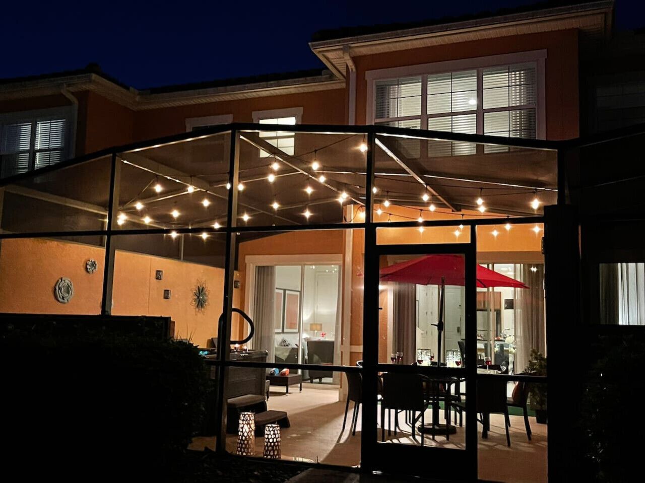 Un patio al aire libre con luces colgantes, un área de estar cubierta y un espacio para comer con un paraguas rojo.