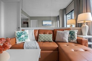 A modern living room with a brown leather sofa, a white coffee table, and a large mirror reflecting the room. - #1604 Lakeview 2/2 condo Next to I-Drive/Universal (Orlando)
