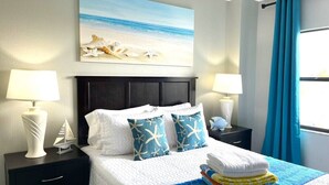 Un letto rifatto con cura, con una coperta a motivi blu e bianchi, due cuscini con decorazioni a stella marina, un piccolo ornamento a forma di vela e una pila di asciugamani piegati.