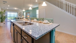 Eine geräumige Küche mit Granit-Arbeitsplatten, einer Spüle mit zwei Becken und Pendelleuchten.