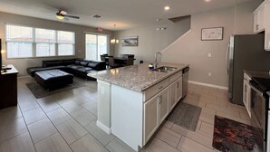 A modern kitchen with a central island, white cabinetry, and a dining area with a black leather couch. - #5135 Cozy Villa 4/4 Centrally Located Disney/Epic (Kissimmee)